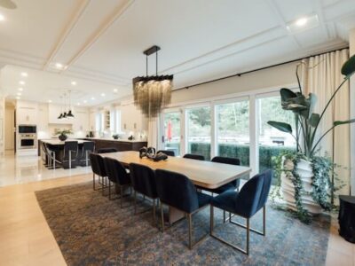 Modern open-plan dining room with wooden table, navy upholstered chairs and a white kitchen in the background