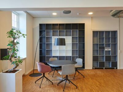Modern office breakout area with a round table, chairs, plants and modular shelving