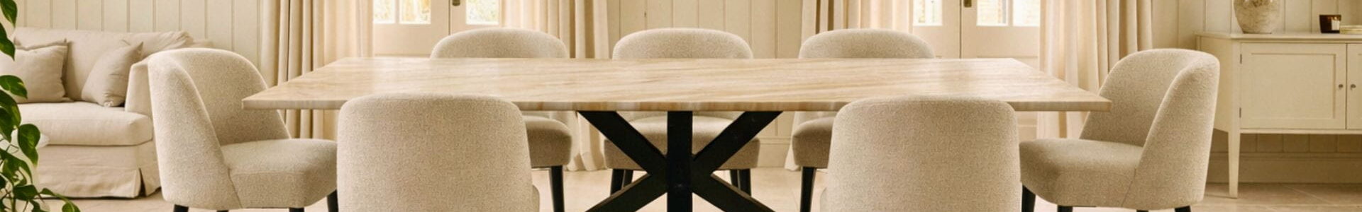 Large dining table with a marble top and black steel X-frame legs surrounded by upholstered chairs